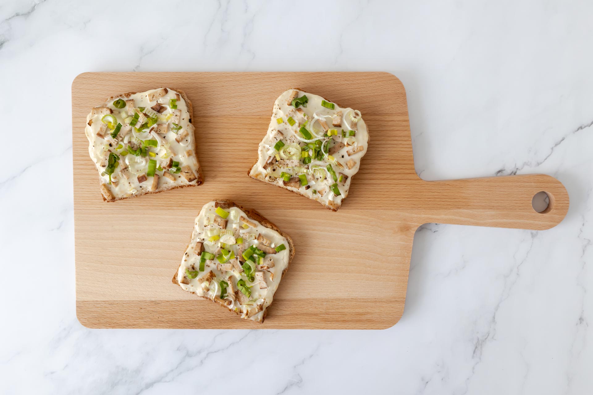 Drei vegane Flammkuchen-Toasts auf Holzbrett – knusprige Apéro-Häppchen mit Räuchertofu, Sauerrahm und Frühlingszwiebeln, von oben fotografiert