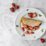 vegane süsse Omeletten mit Erdbeeren auf dem Teller dekoriert mit Pistazien