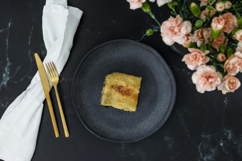 Spinat Lasagne vegan von oben mit Blumen und goldenem Besteck und weisser Serviette