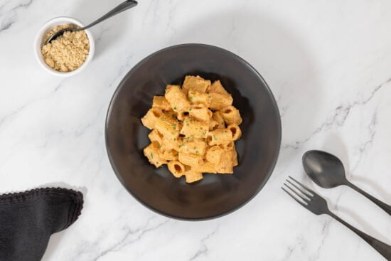 Rigatoni mit Tahini-Tomaten-Pesto Vegan mit Nuss Parmesan und Besteck auf dem Teller