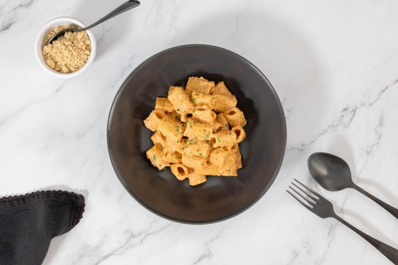Rigatoni mit Tahini-Tomaten-Pesto Vegan mit Nuss Parmesan und Besteck auf dem Teller