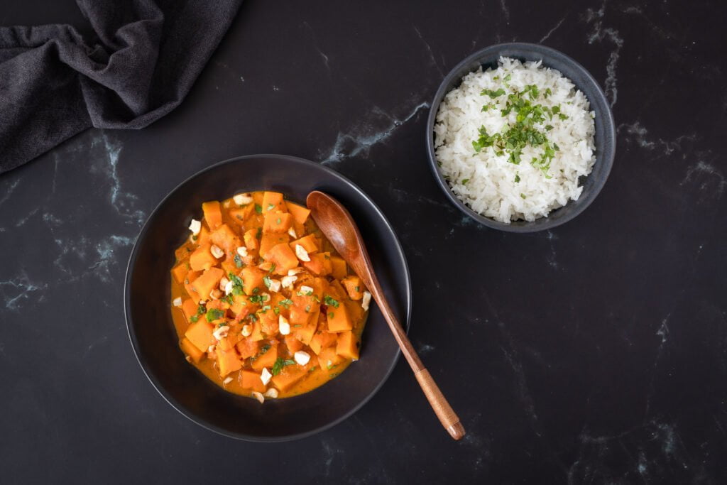 Veganes Kuerbis Curry mit Loeffel im Teller und Servette daneben