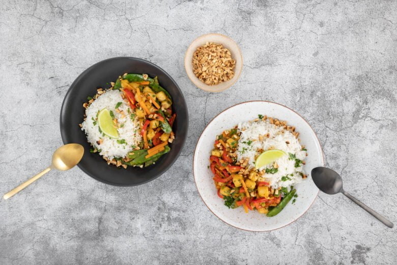 Thai Curry mit Erdnüssen und Limette auf zwei Tellern auf dem Tisch mit geschnittenen Erdnüssen