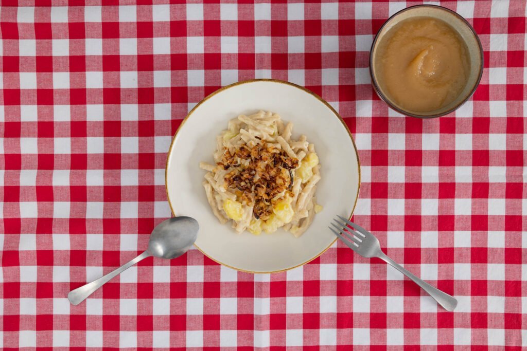 Vegane Älplermagronen mit Röstzwiebeln und Apfelmus – traditionelles Schweizer Gericht als pflanzliche Version, serviert mit Gabel auf Serviette
