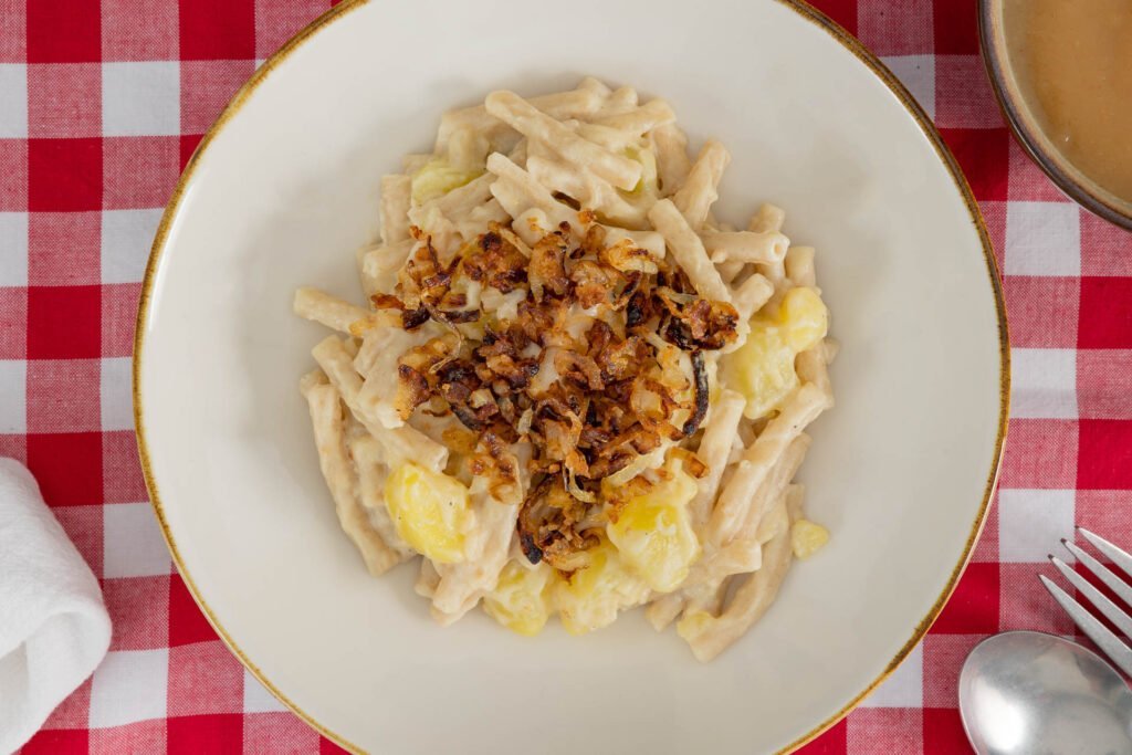 Detailaufnahme von Älplermagronen vegan – cremige Magronen mit Röstzwiebeln im Teller, Schweizer Küche ohne Käse