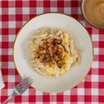 Vegane Älplermagronen Nahaufnahme – Magronen mit Röstzwiebeln und Apfelmus, serviert mit Gabel, inspiriert von Schweizer Bergküche