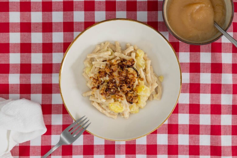 Vegane Älplermagronen Nahaufnahme – Magronen mit Röstzwiebeln und Apfelmus, serviert mit Gabel, inspiriert von Schweizer Bergküche