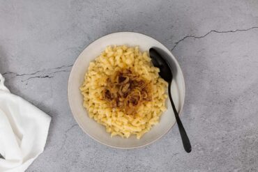 Knöpfli ohne Ei mit gerösteten Zwiebeln im Teller mit Löffel.