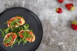 Tomaten Erdbeer Bruschetta mit Cashewcreme auf einem Teller mit Erdbeeren als Deko