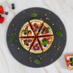Melonen Pizza auf einem schwarzen Teller mit Fruechten und einem Stueck