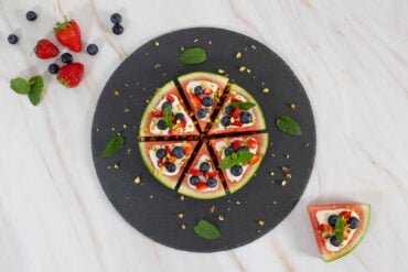 Melonen Pizza auf einem schwarzen Teller mit Fruechten und einem Stueck