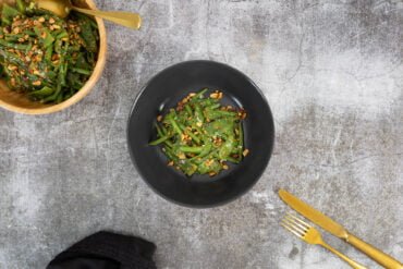 Bohnensalat mit Ingwer und Erdnuessen auf schwarzem Teller