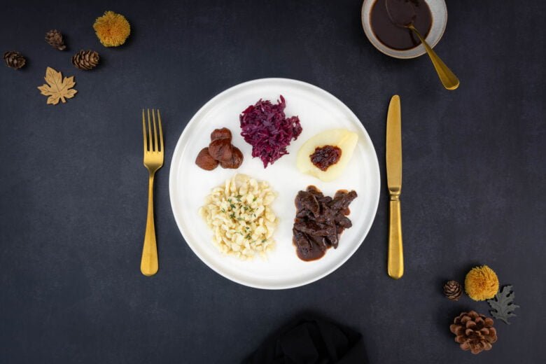 Veganer Wildteller - Kastanien Spätzli Wild mit Rotkraut und Herbstdekoration und Saucenschale auf dem Tisch