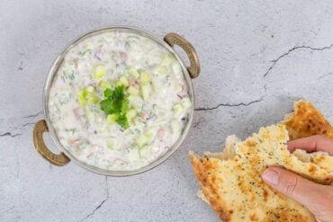 Veganes Raita - indische Joghurtsauce mit Gurke und Tomate alle Zutaten werden in die Schüssel gegeben beim Kochen