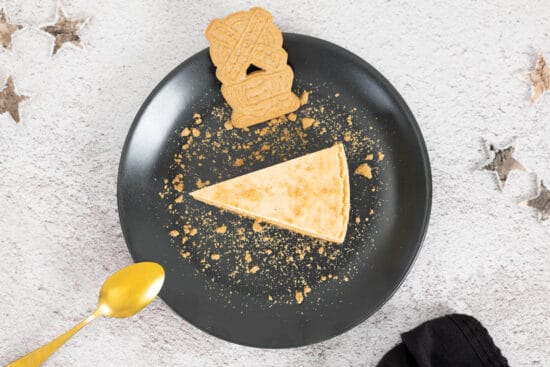 Veganer Spekulatius Cheesecake auf dem Teller mit Spekulatius und Weihnachts-Deko und Löffel auf dem Teller