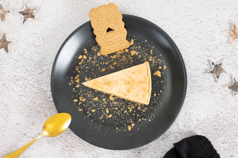 Veganer Spekulatius Cheesecake auf dem Teller mit Spekulatius und Weihnachts-Deko und Löffel auf dem Teller