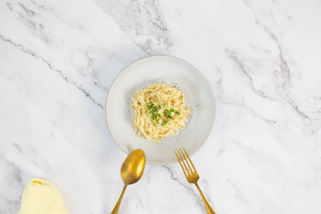 Cremige vegane Tagliatelle al Limone – Zitronenpasta mit Petersilie und schwarzem Pfeffer, angerichtet mit goldenem Besteck
