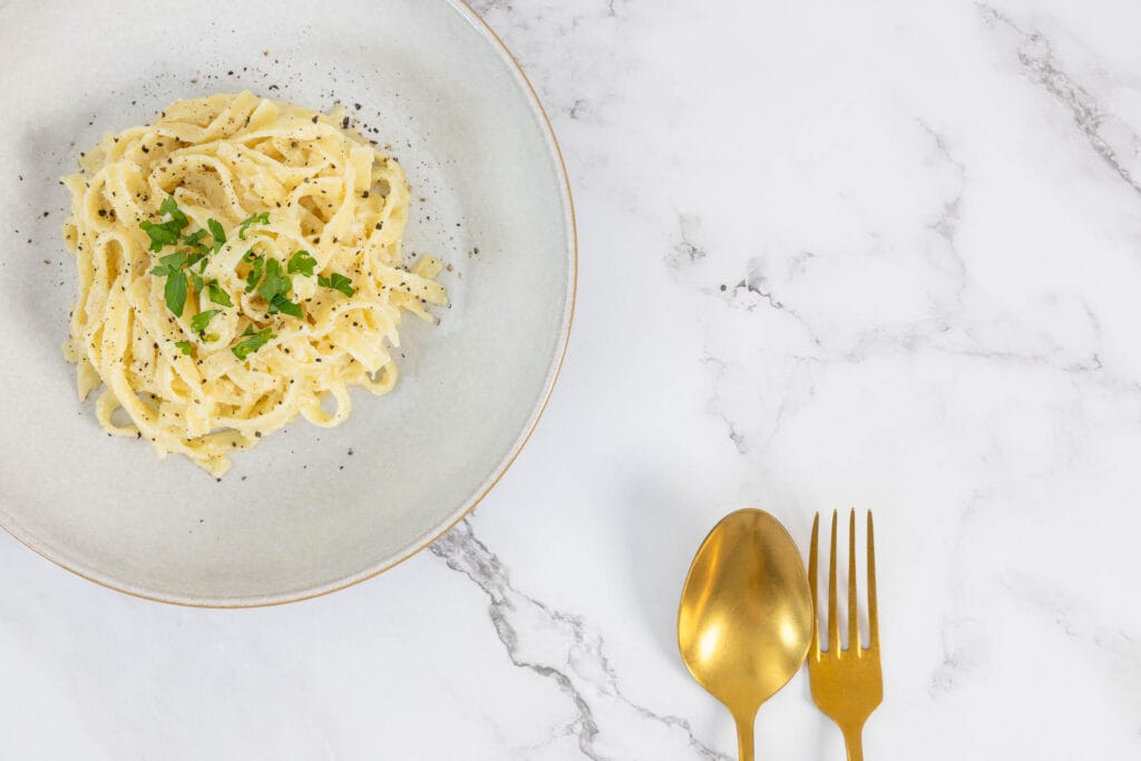 Teller mit veganer Zitronenpasta – Tagliatelle al Limone mit Petersilie garniert und Pfeffer bestreut