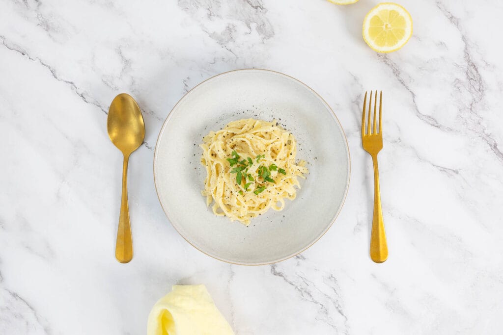 Zitronenpasta vegan – Tagliatelle al Limone mit Petersilie, frischer Zitrone und goldfarbenem Besteck von oben fotografiert