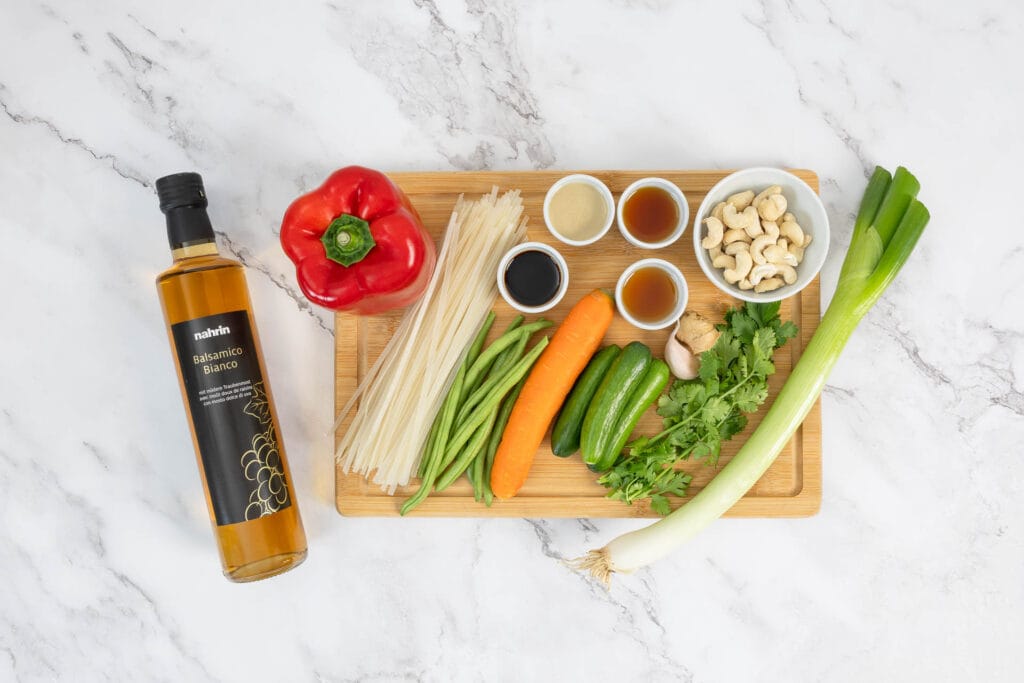 Zutaten für asiatischen Nudelsalat mit grünen Bohnen und Reisnudeln auf Holzbrett, mit Balsamico Bianco Essigflasche