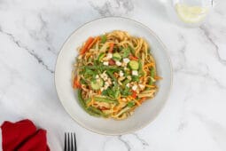 Asiatischer Nudelsalat mit grünen Bohnen im Teller, Glas Wasser im Bild, Draufsicht
