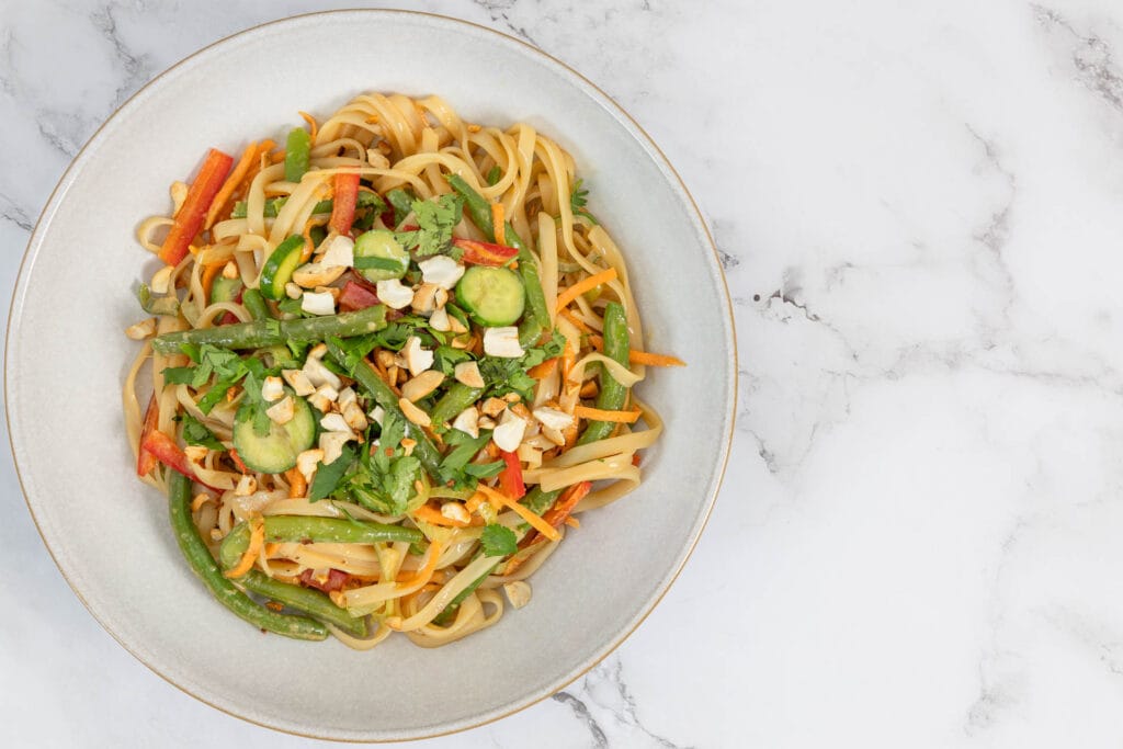 Asiatischer Nudelsalat mit grünen Bohnen, Reisnudeln und Cashews im Teller von oben