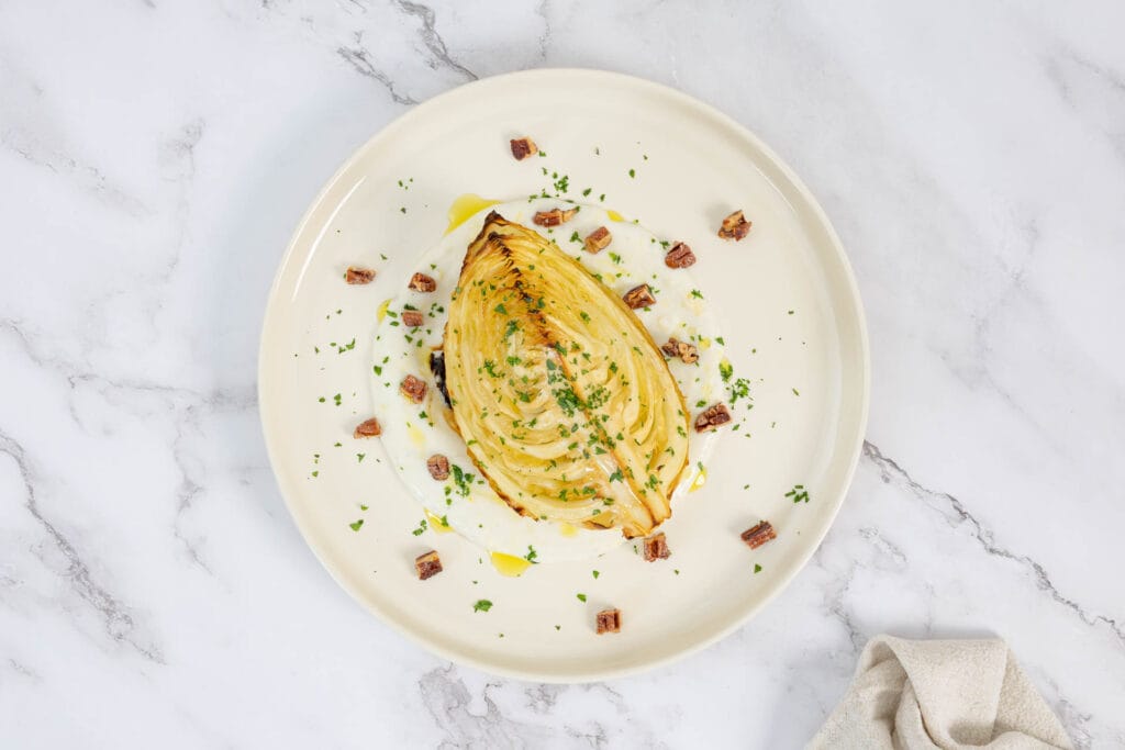 Nahaufnahme gebackene Kabisspalten auf Joghurtsauce mit Petersilie und gebrannten Nüssen, veganes Ofenrezept