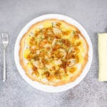 Vegane Kartoffelpizza mit Birne und karamellisierten Zwiebeln serviert auf Teller mit Besteck – Pizza Bianca vegan