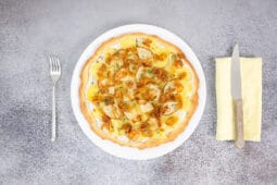 Vegane Kartoffelpizza mit Birne und karamellisierten Zwiebeln serviert auf Teller mit Besteck – Pizza Bianca vegan