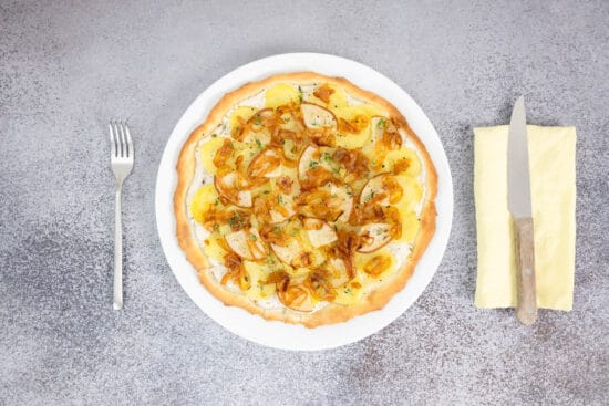 Vegane Kartoffelpizza mit Birne und karamellisierten Zwiebeln serviert auf Teller mit Besteck – Pizza Bianca vegan