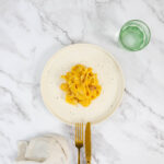 Cremige Kürbispasta serviert mit Glas Wasser und Besteck – so schmeckt Alfredo im Herbst, leicht und aromatisch