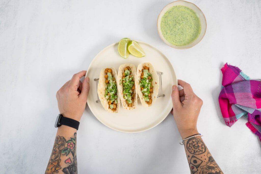 Kichererbsen-Tacos mit Koriander-Sauce, serviert auf Teller – Hände halten das Gericht, mexikanisches Streetfood zuhause geniessen