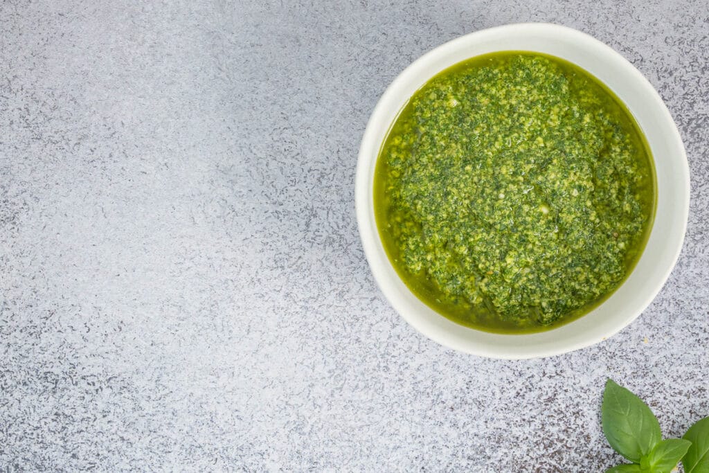 Detailaufnahme: Schüssel mit hausgemachtem veganem Basilikum-Pesto, Basilikumblatt am Rand, leuchtend grün und voller Aroma