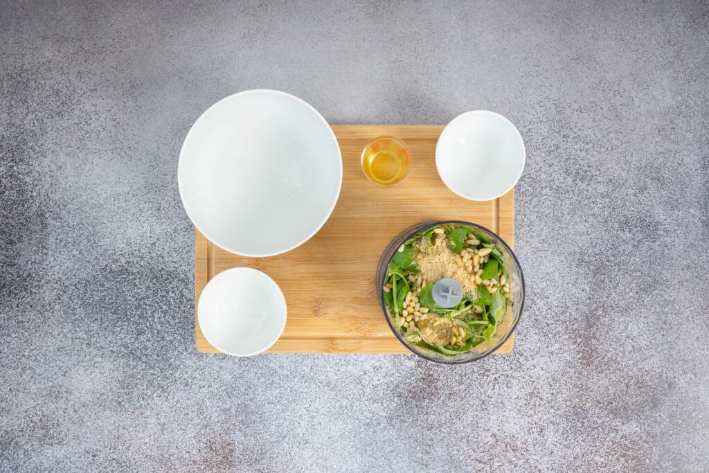 Zutaten für veganes Pesto Genovese im Behälter des Food Processors – Basilikum, Pinienkerne, Olivenöl und Hefeflocken bereit zum Mixen