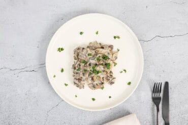 Veganer Pilztoast mit Petersilie auf einem Teller, daneben Gabel, Messer und Serviette