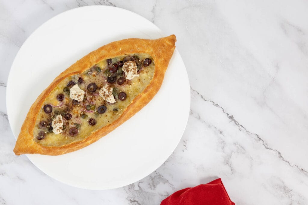 Gebackenes veganes Pide mit Oliven, Zaatar und Ricotta – serviert auf Teller mit roter Serviette