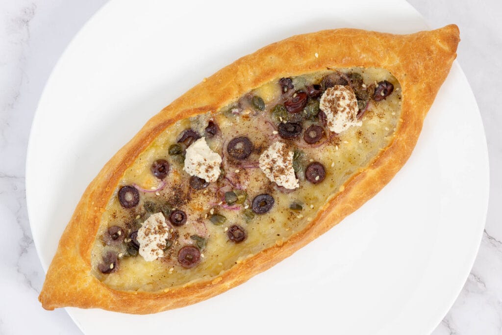 Nahaufnahme von veganem Pide mit Zaatar und Oliven – goldbrauner Rand und cremiger Ricotta