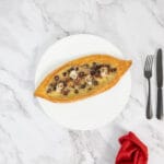 Veganes Pide mit Oliven und Zaatar – serviert mit roter Serviette und schwarzem Besteck auf hellem Teller