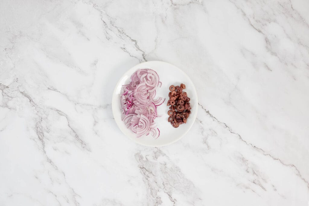 Geschnittene Zwiebeln und Oliven als Belag für veganes Pide mit Zaatar und Kapern