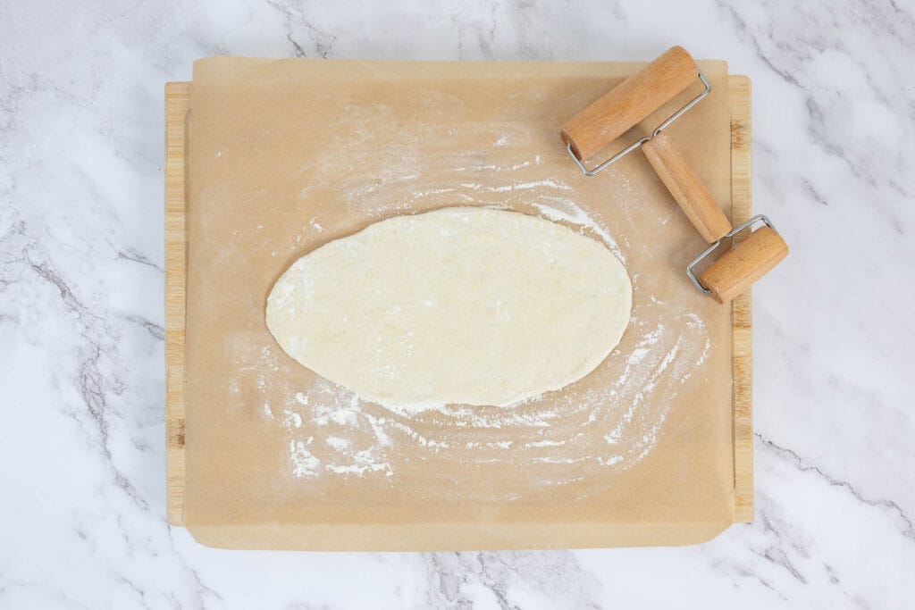 Ausgerollter Pide-Teig in ovaler Form auf bemehltem Brett mit Teigroller – Vorbereitung fürs Belegen
