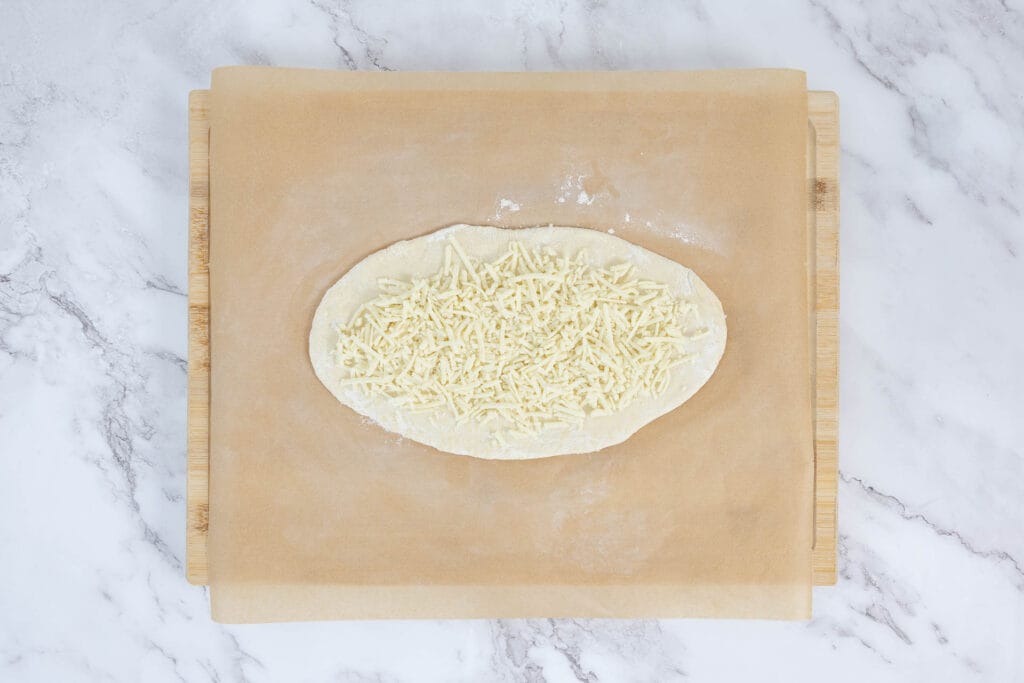 Pide-Teig oval ausgerollt und mit veganem Reibkäse belegt – Schritt zur Füllung des veganen Pide