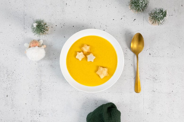 Vegane Rüebli-Chili-Suppe mit Vanille von oben, angerichtet mit Stern-Croûtons, goldener Löffel und winterliche Dekoration.