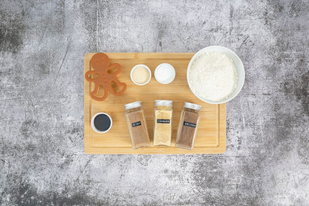 Zutaten für vegane Gingerbread Men auf Holzbrett mit Mehl, Zucker, Birnel, Gewürzen und Ausstecher – Grundlage für ein veganes Gingerbread-Men-Rezept