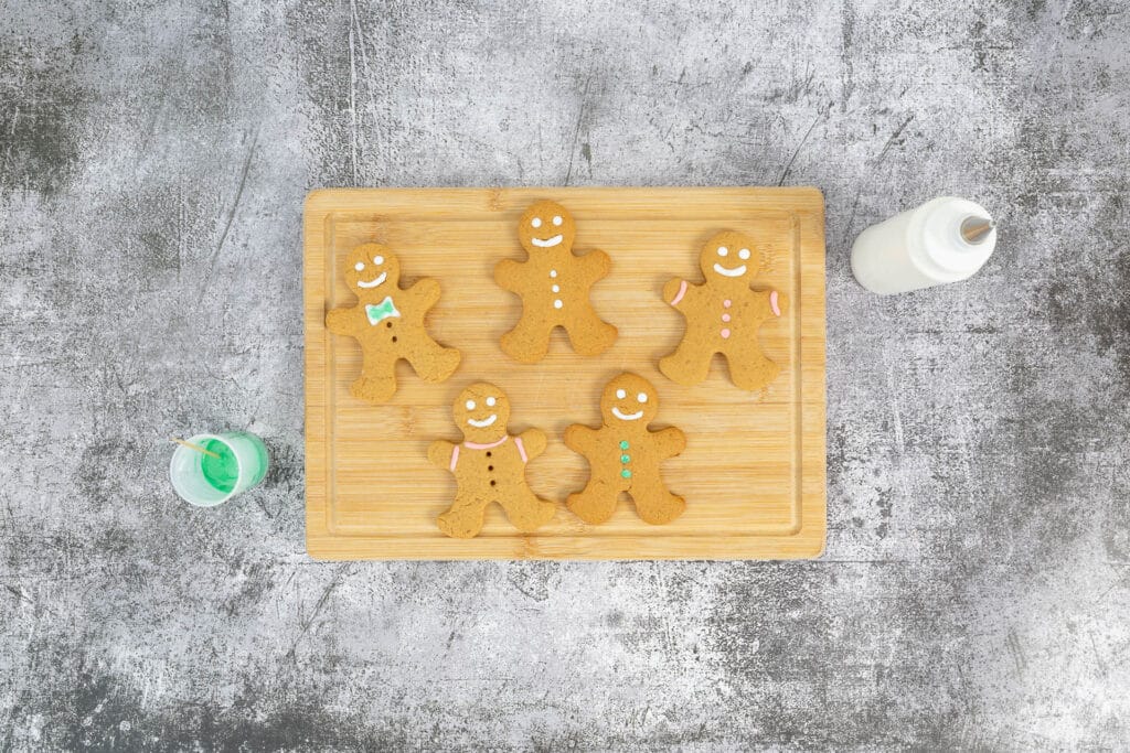 Fünf dekorierte vegane Gingerbread Men mit Spritzflasche und grünem Zuckerguss auf Holzbrett – weihnachtliches Lebkuchenmännchen-Verzieren