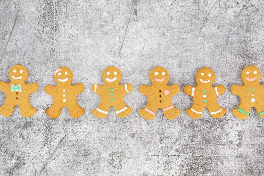 Sieben vegan dekorierte Gingerbread Men nebeneinander vor grauem Hintergrund – klassisch weihnachtlich