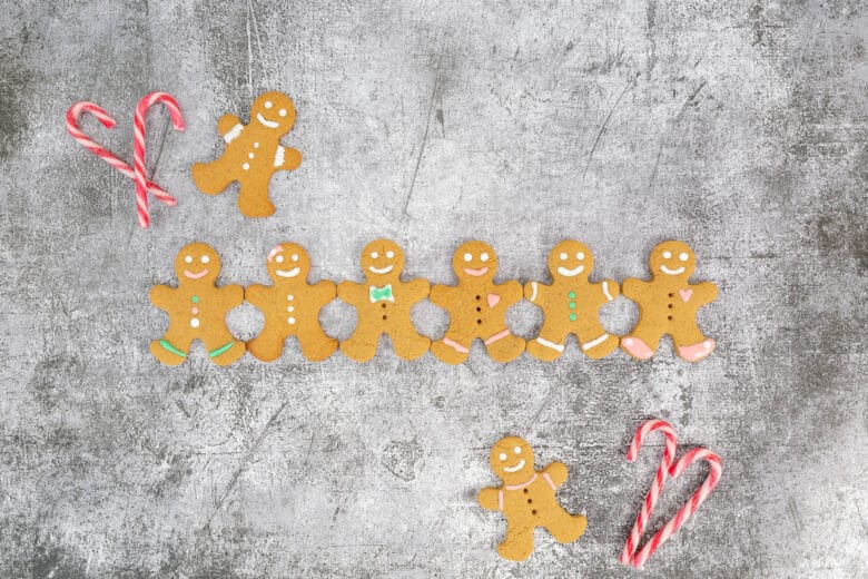 Acht dekorierte vegane Gingerbread Men auf grauem Hintergrund, umgeben von Candy Canes in Herzform – perfektes veganes Weihnachtsguetzli-Motiv