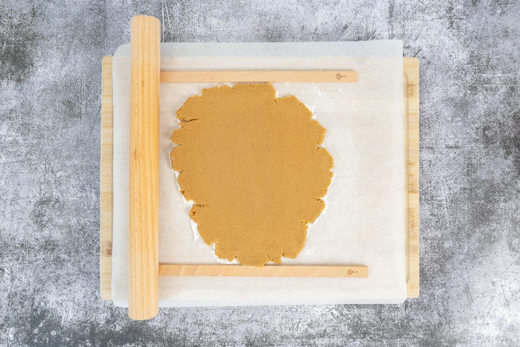 Ausgerollter veganer Gingerbread-Teig zwischen Backpapier mit Abstandshölzern – ideal zum gleichmässigen Ausrollen und Ausstechen