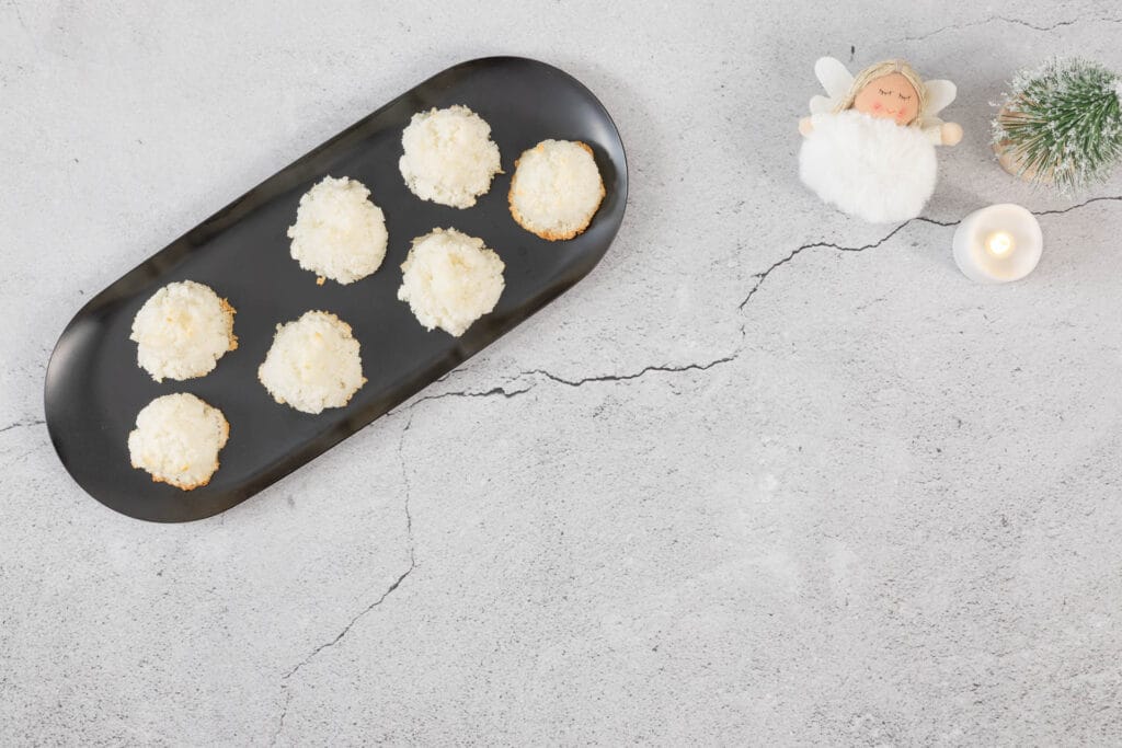 Seitliche Weihnachtsdeko mit Engel und Mini-Tannen rund um eine Platte mit veganen Kokosmakronen, glutenfrei und einfach gemacht