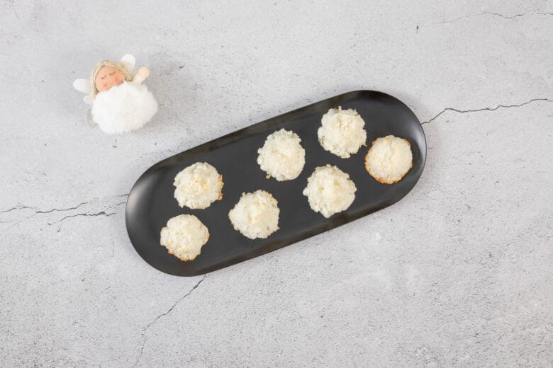 Kokosmakronen auf schwarzer Platte, dekoriert mit einem kleinen Weihnachtsengel für festliche vegane Guetzli-Inspiration