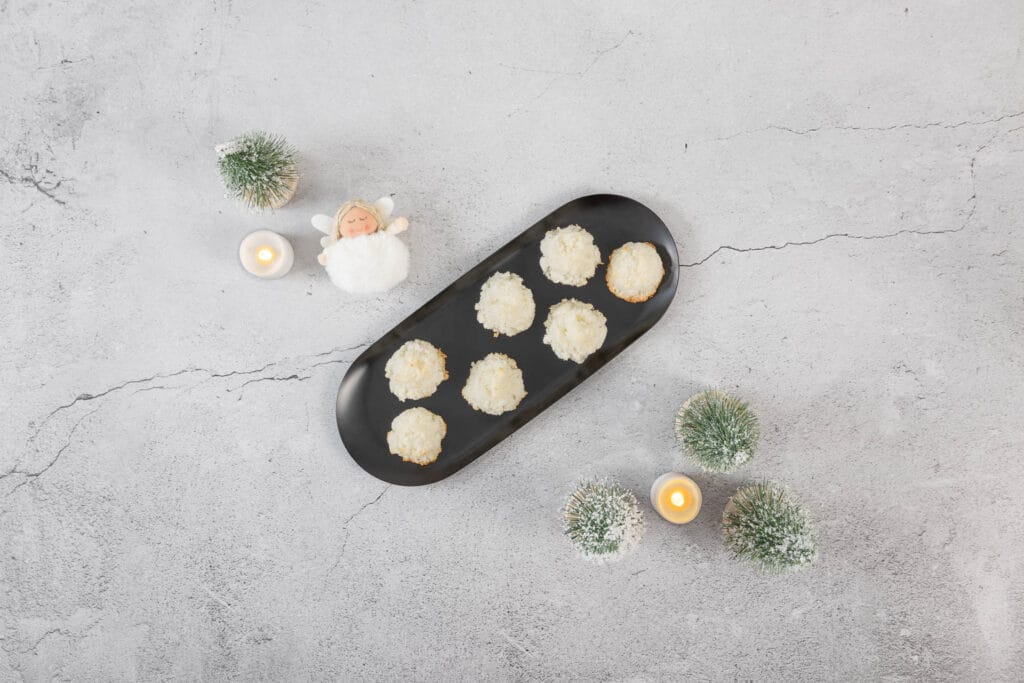 Festlich präsentierte vegane Kokosmakronen auf schwarzer Platte mit Kerzen und winterlicher Deko